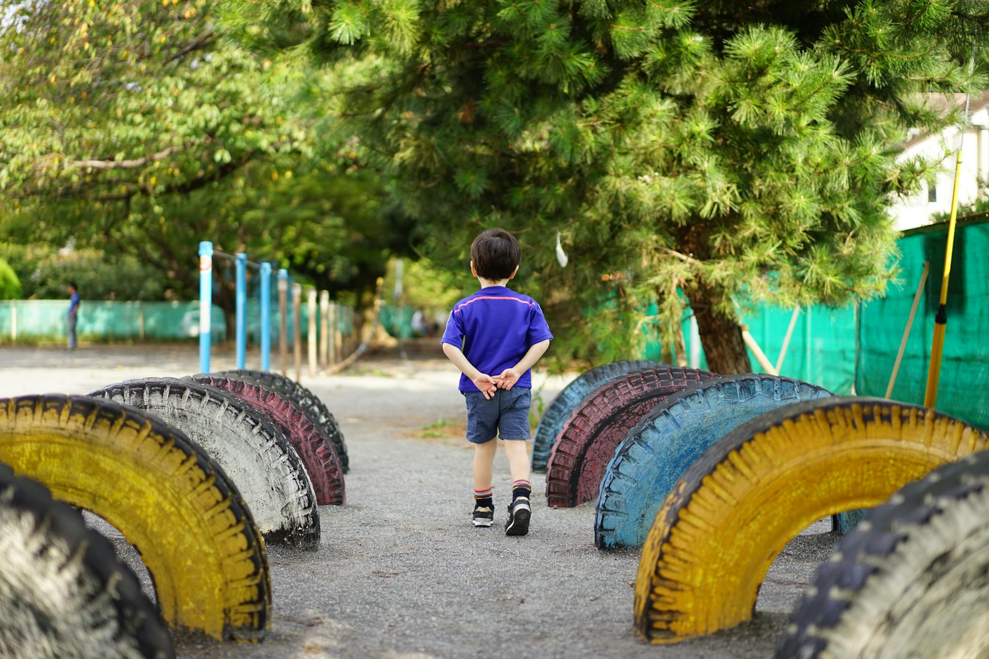 A young child walks through a playground with colorful tire arches, exploring a sunny day outdoors.