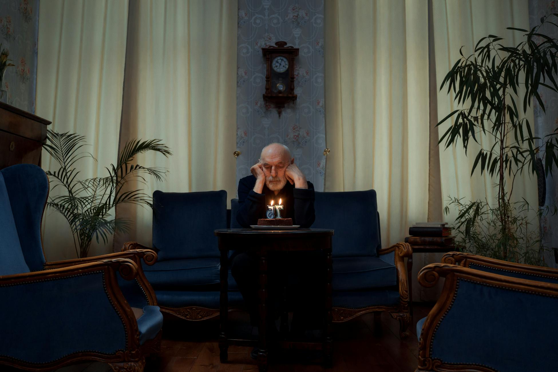 Senior man alone with a birthday cake in a vintage living room setting.
