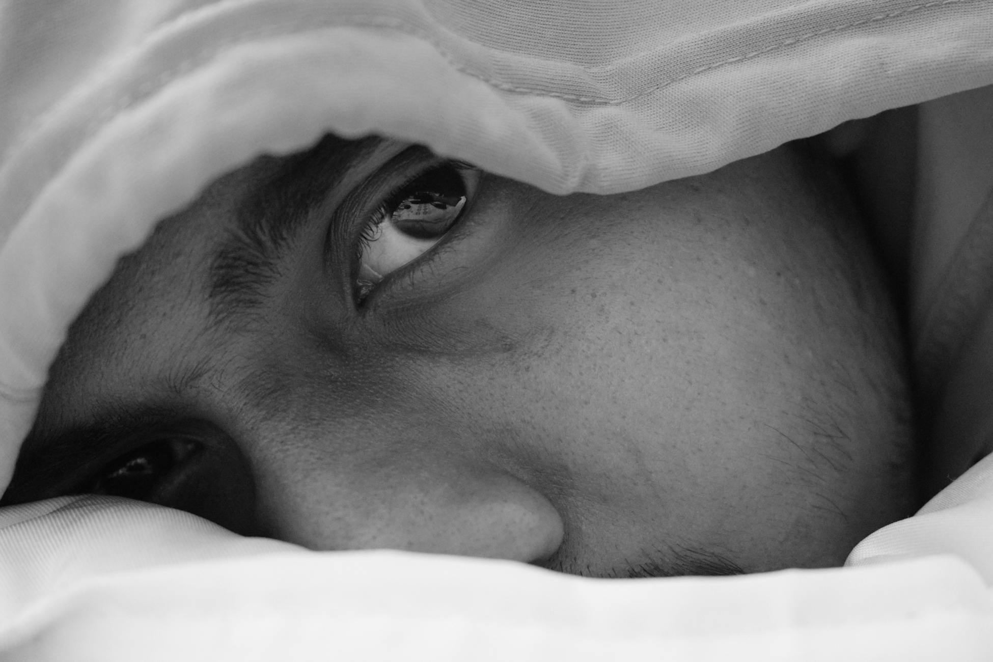 A contemplative black and white close-up of a man gazing thoughtfully, partially covered by a duvet.