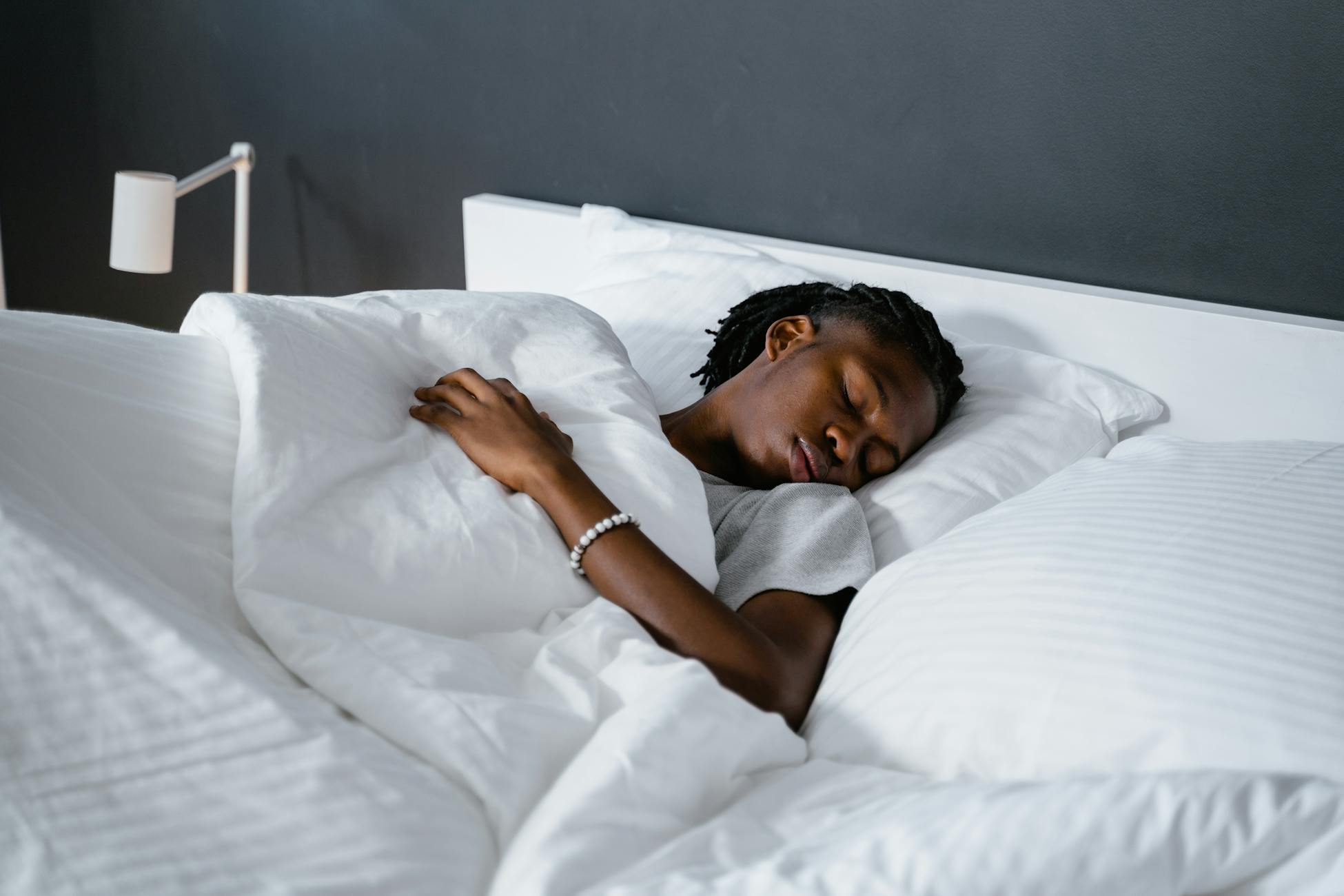A man sleeping peacefully under a white blanket in a cozy bedroom.