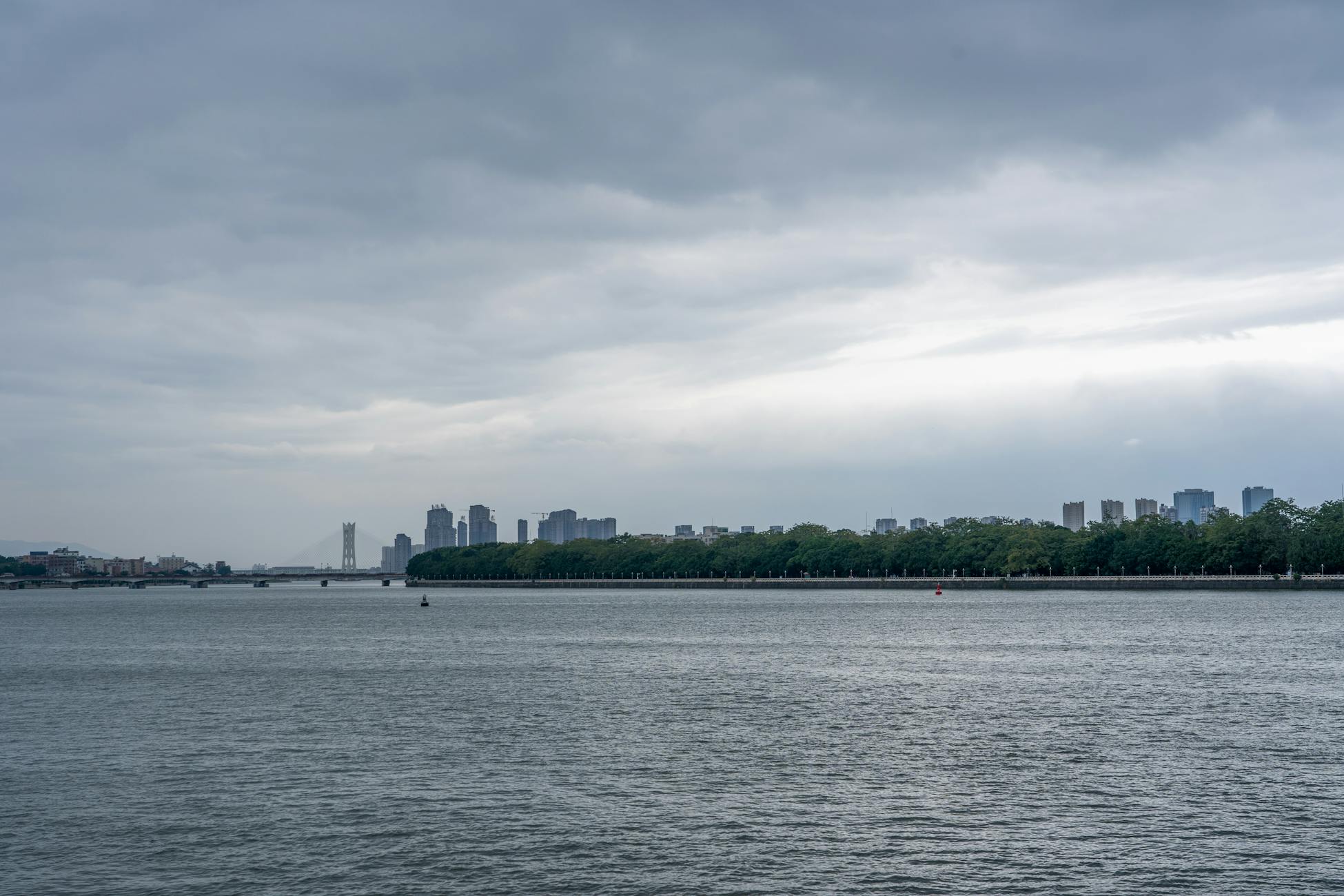 A serene view of a cityscape with a river and cloudy sky, showcasing modern architecture.