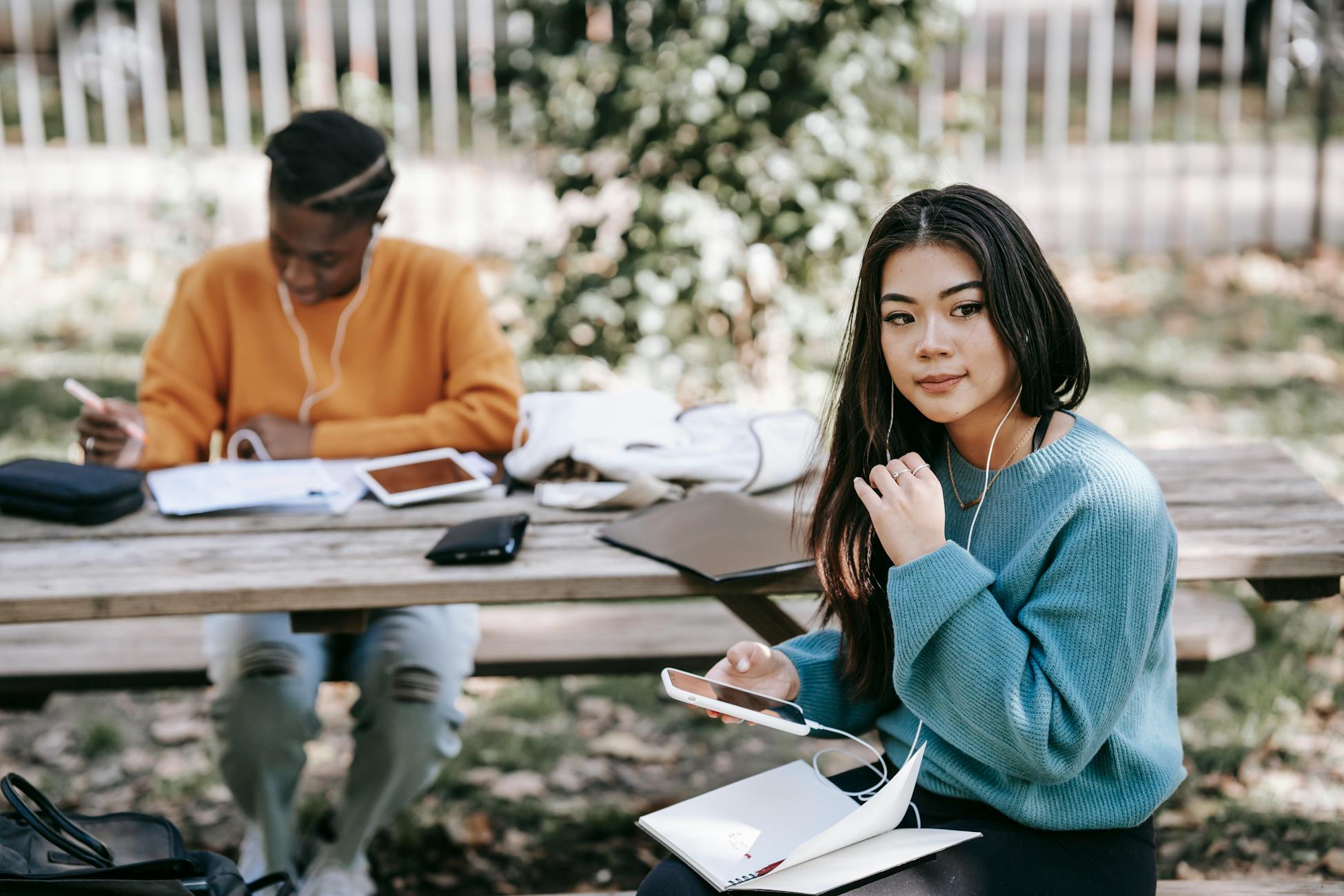 Pensive young multiethnic students working together with notebooks at table on blurred background of street