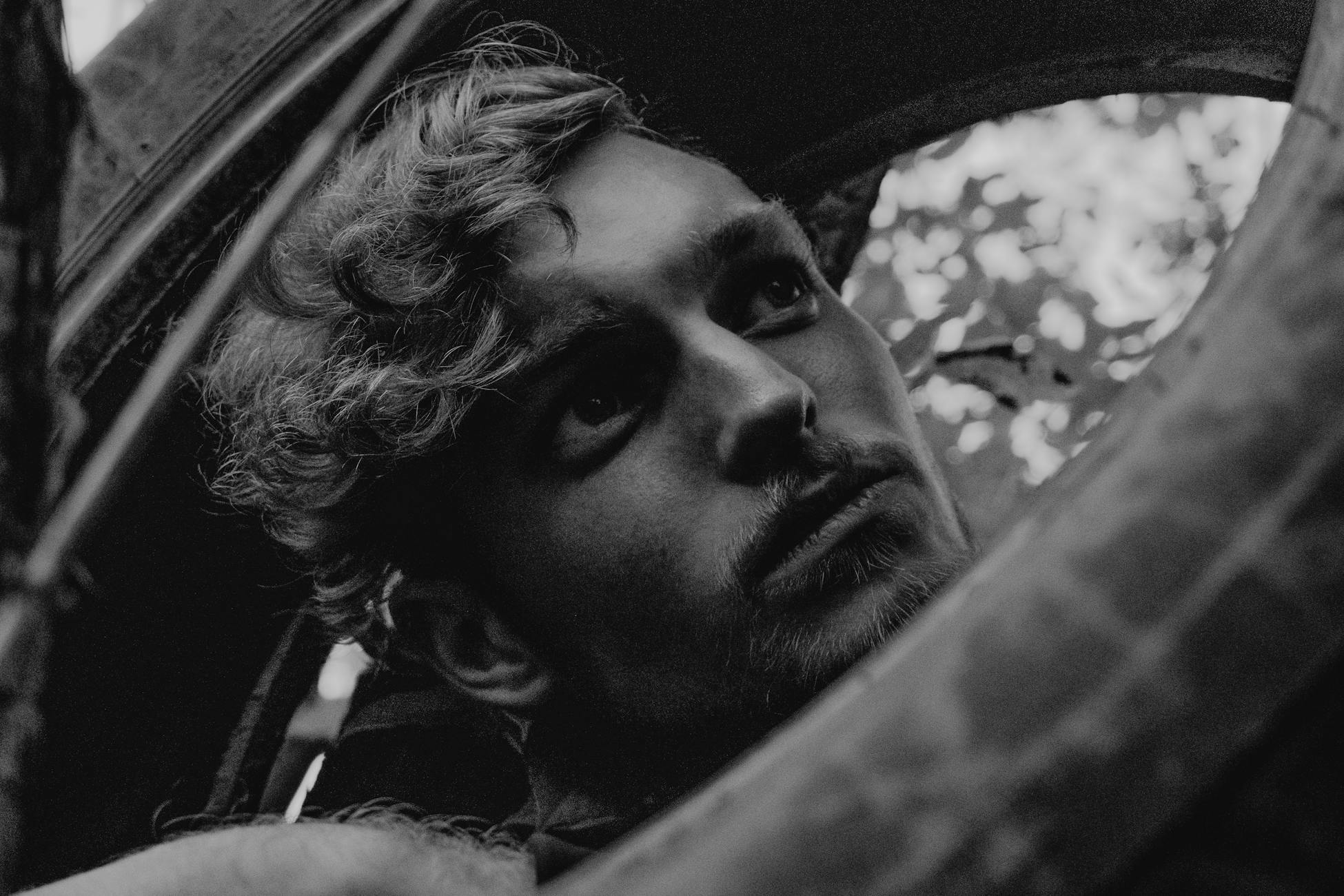 A moody black and white close-up of a man looking thoughtfully to the distance.