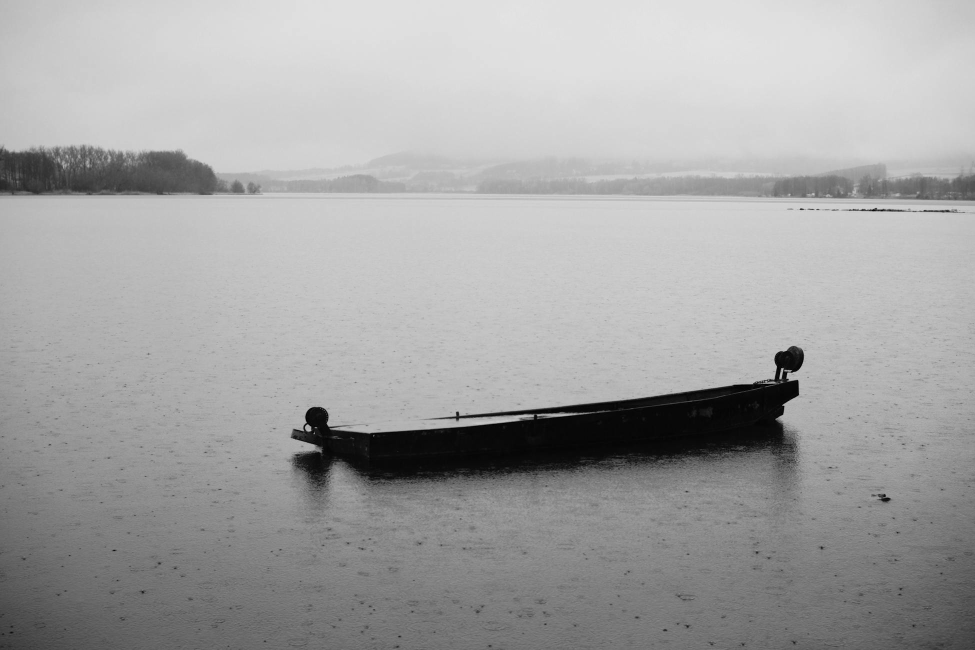 Monochrome image of a lone boat floating on a tranquil lake, evoking solitude.