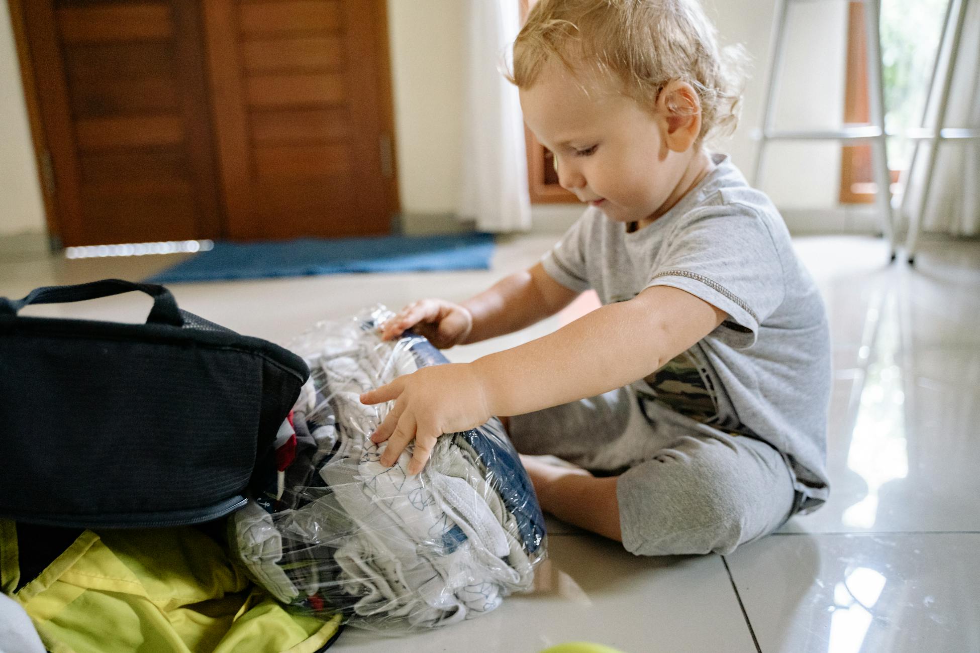 A toddler sitting on the floor playing with clothes in a plastic bag indoors.