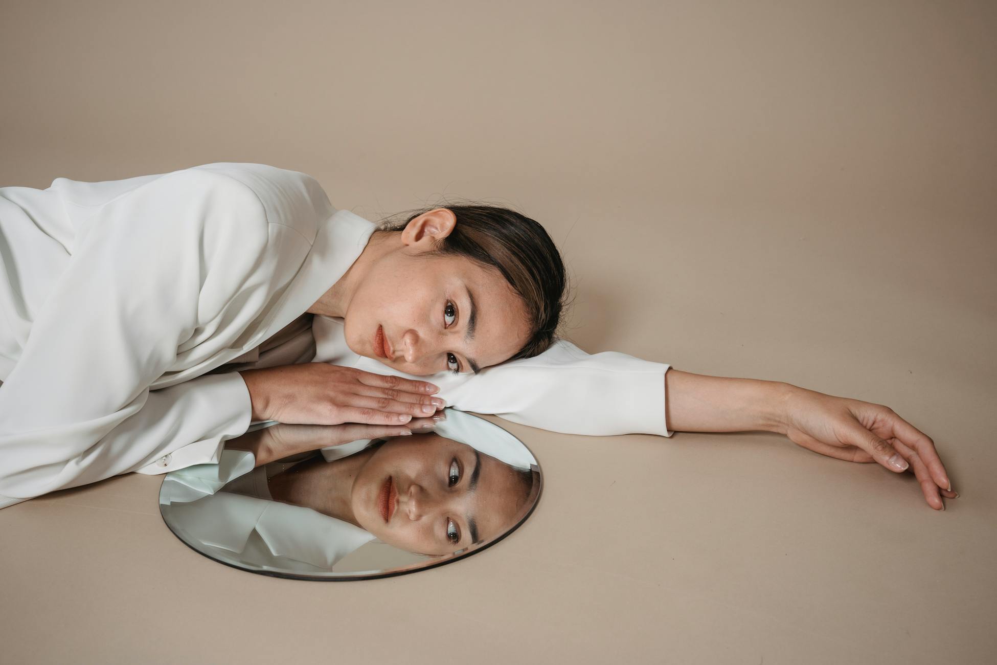 Stylish woman in white suit lying beside mirror, reflecting beauty and elegance.