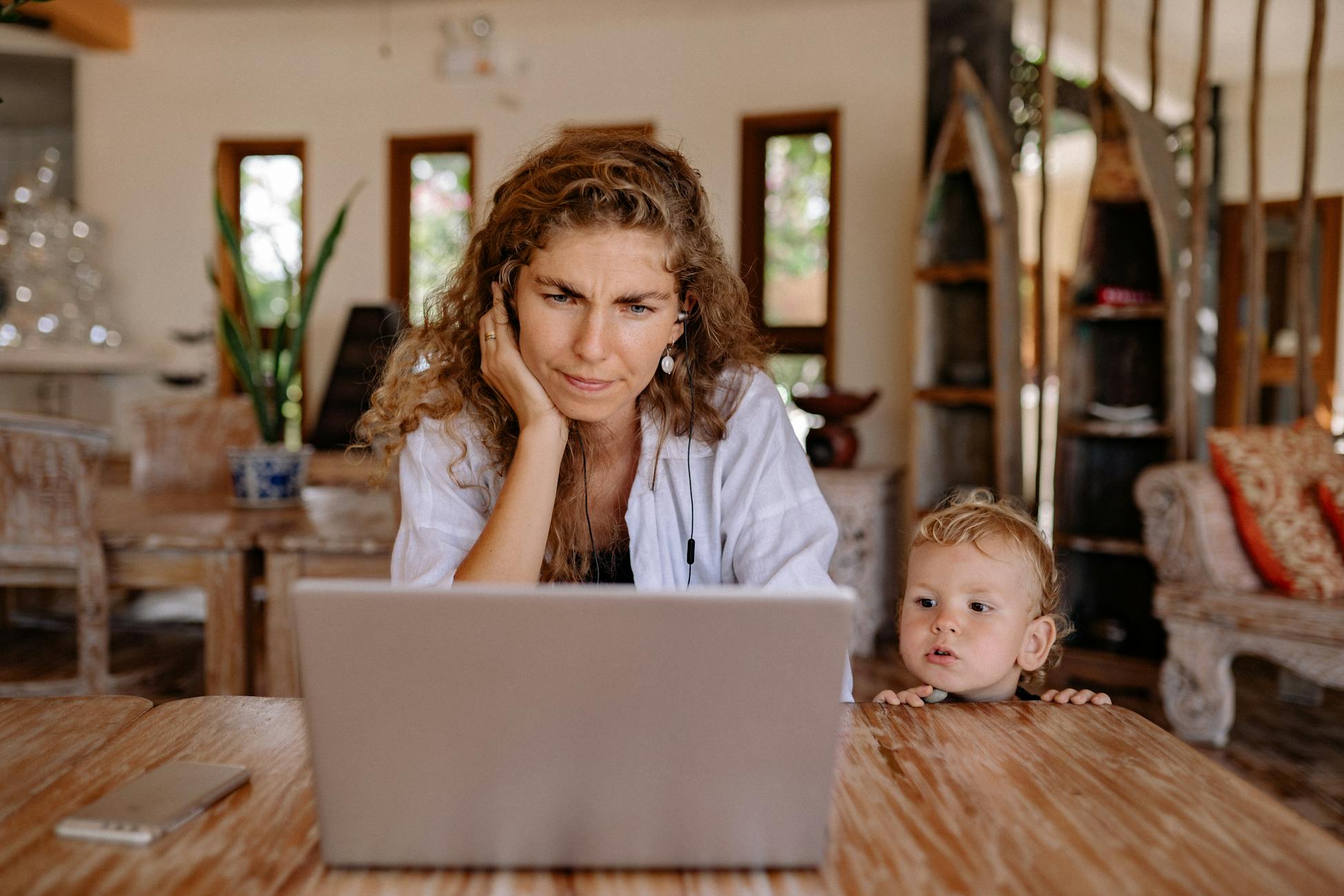 Mother and young son using a laptop at a cozy wooden table indoors.