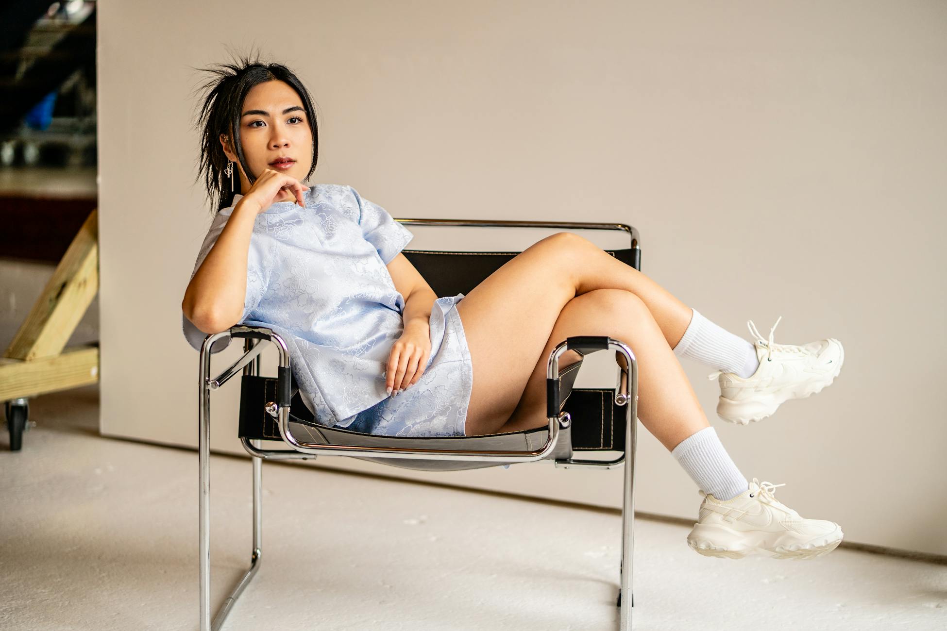 Stylish Asian woman reclining in a chic chair, exuding modern elegance in a studio setting.
