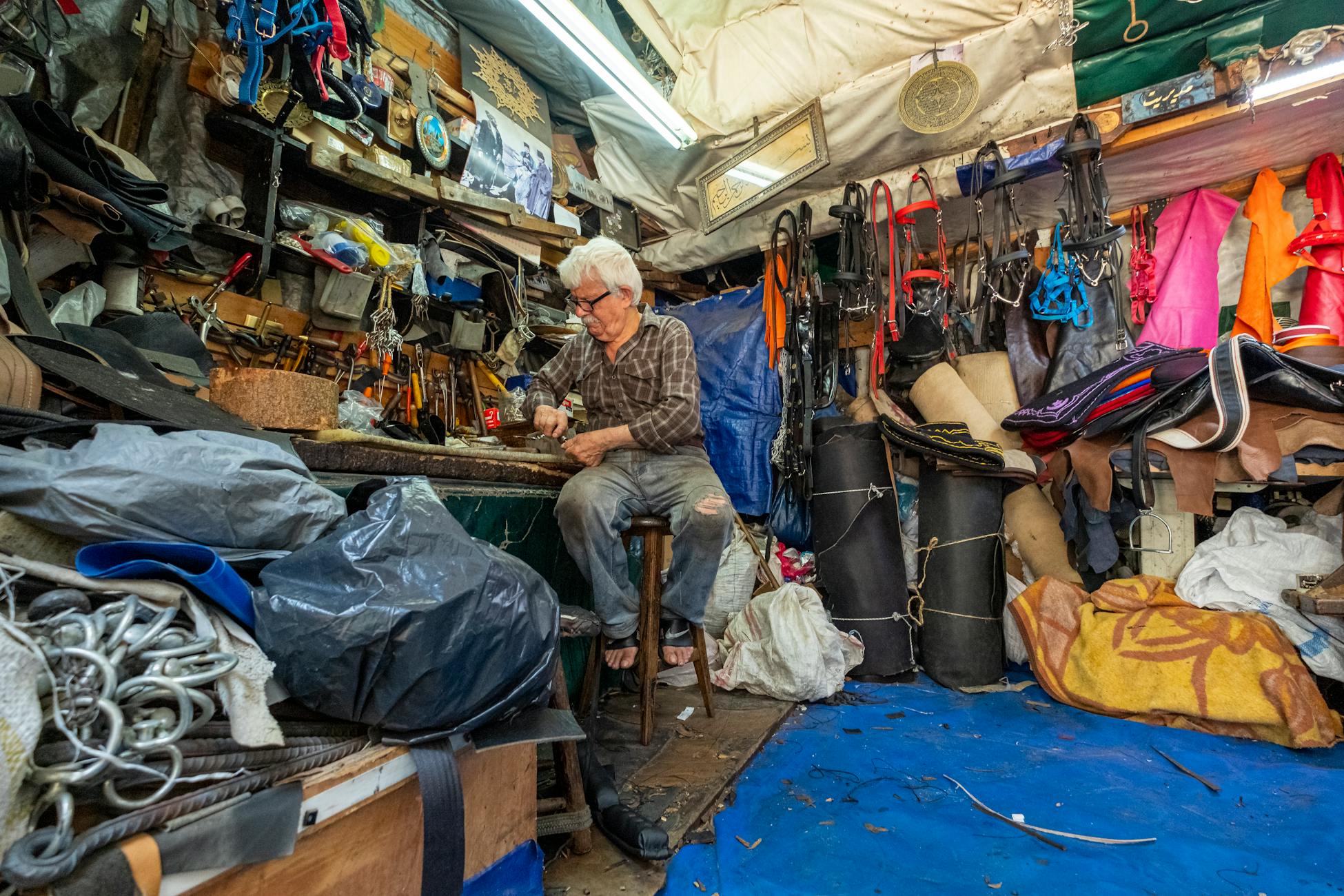 Senior craftsman focuses on detailed work amidst a packed workshop environment.