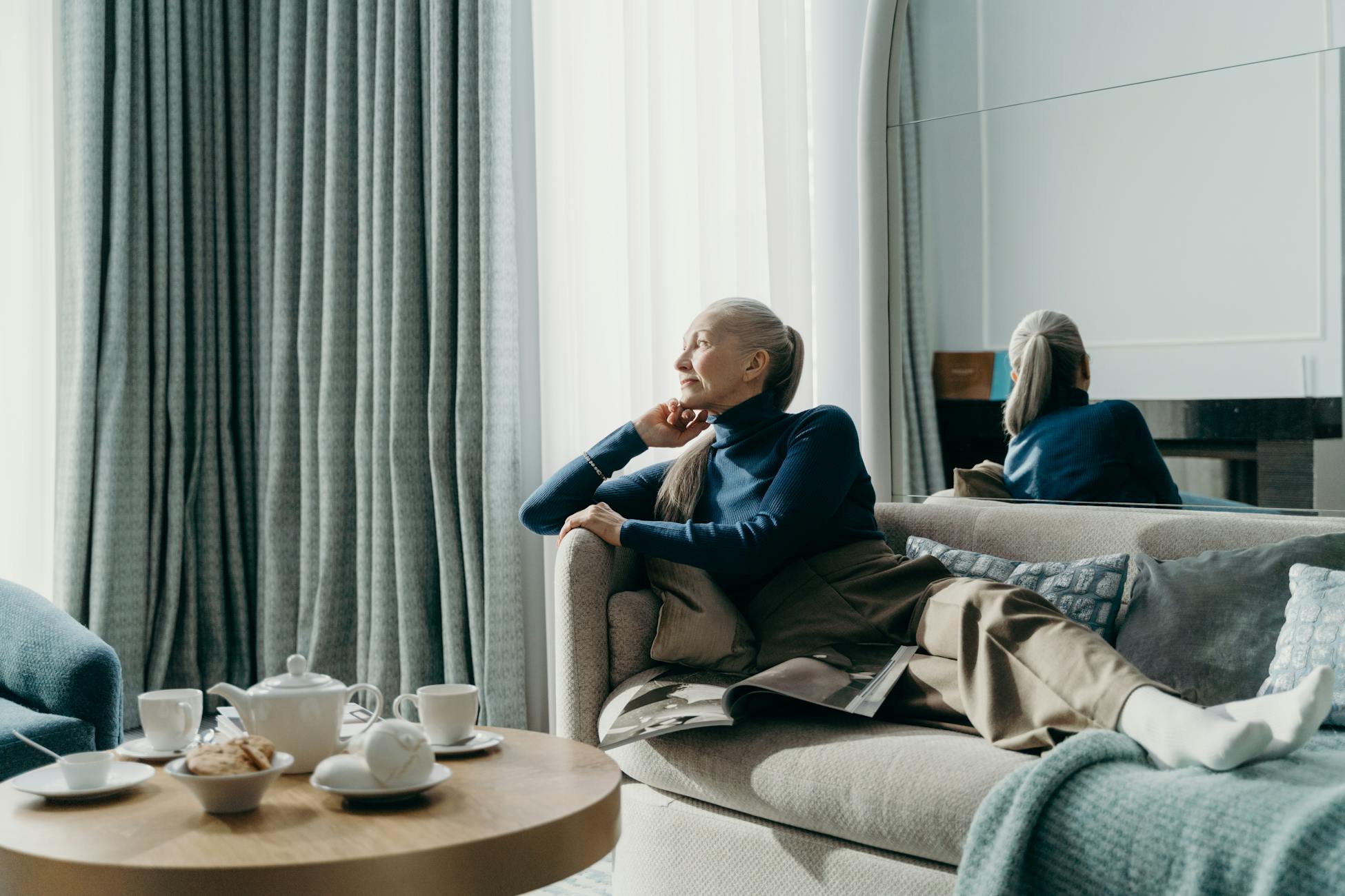 Senior woman sitting on a couch, contemplating and relaxing with a cup of tea.