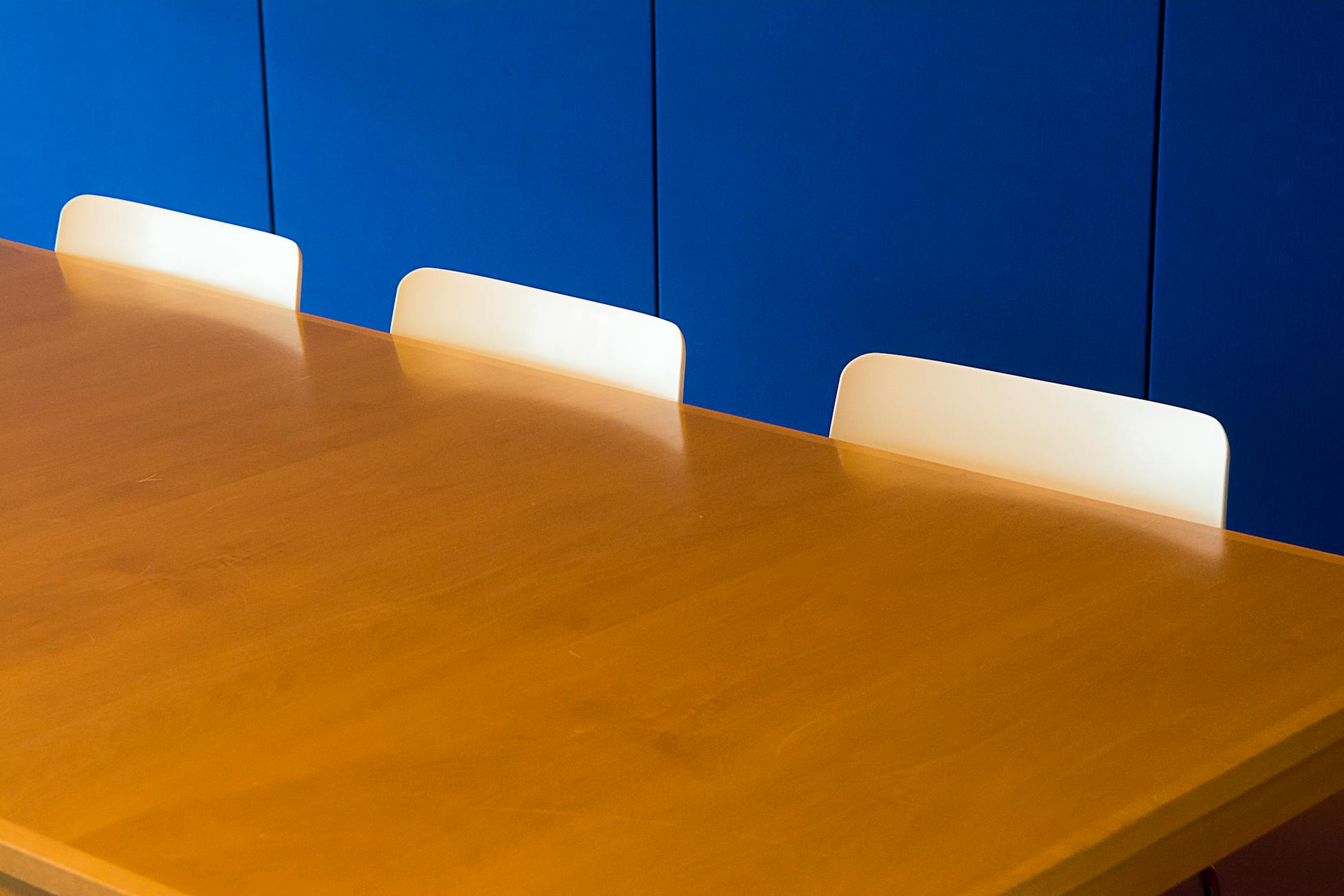 A clean and modern indoor meeting room with a wooden table against a blue wall.