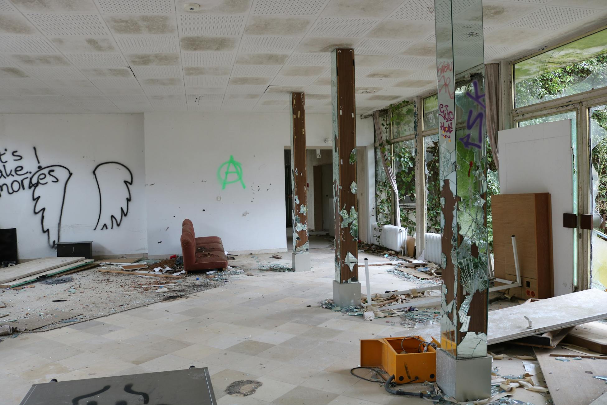 An abandoned room with broken windows, graffiti on white walls, and scattered debris.