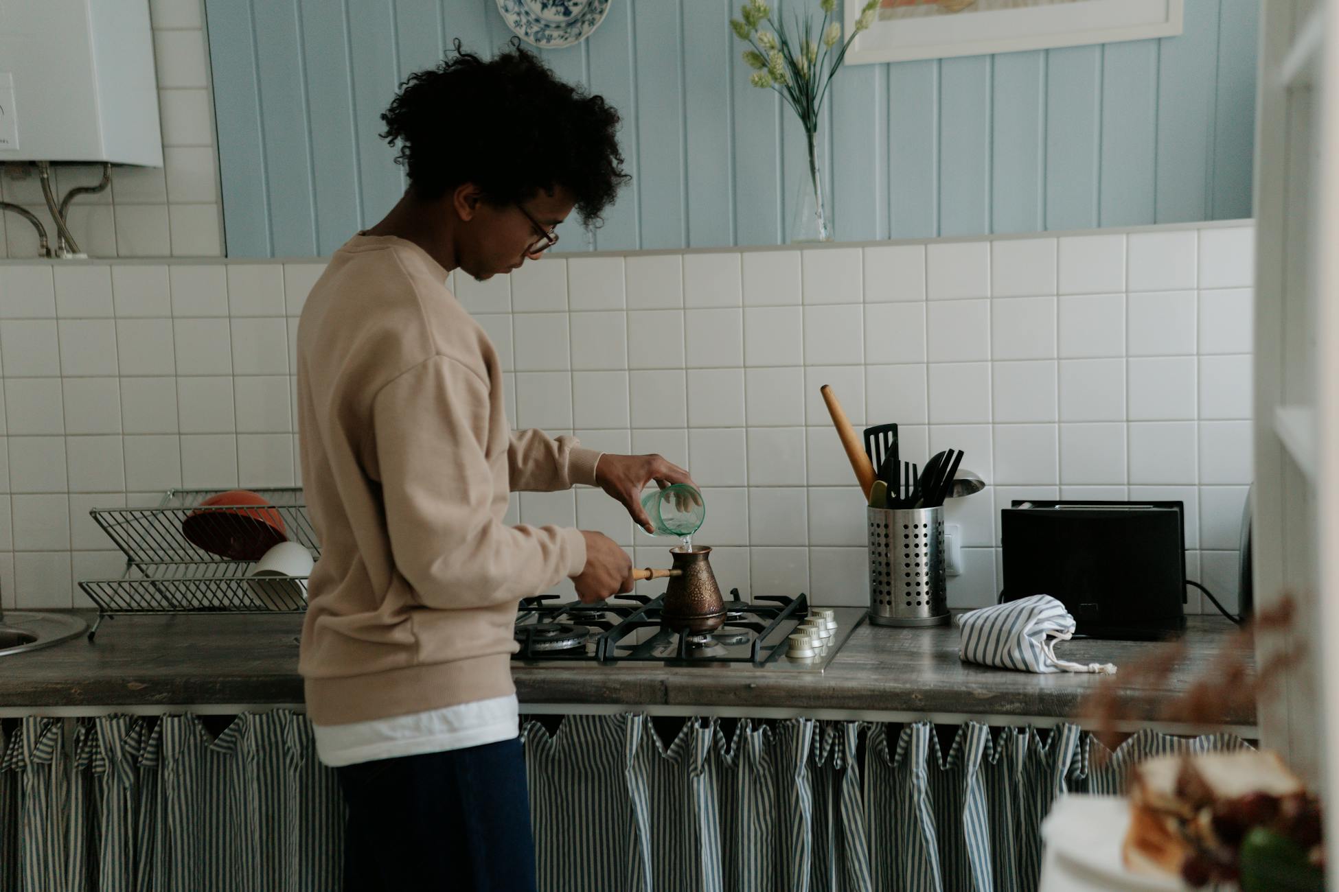 A young man making coffee on a gas stove in a cozy kitchen setting.