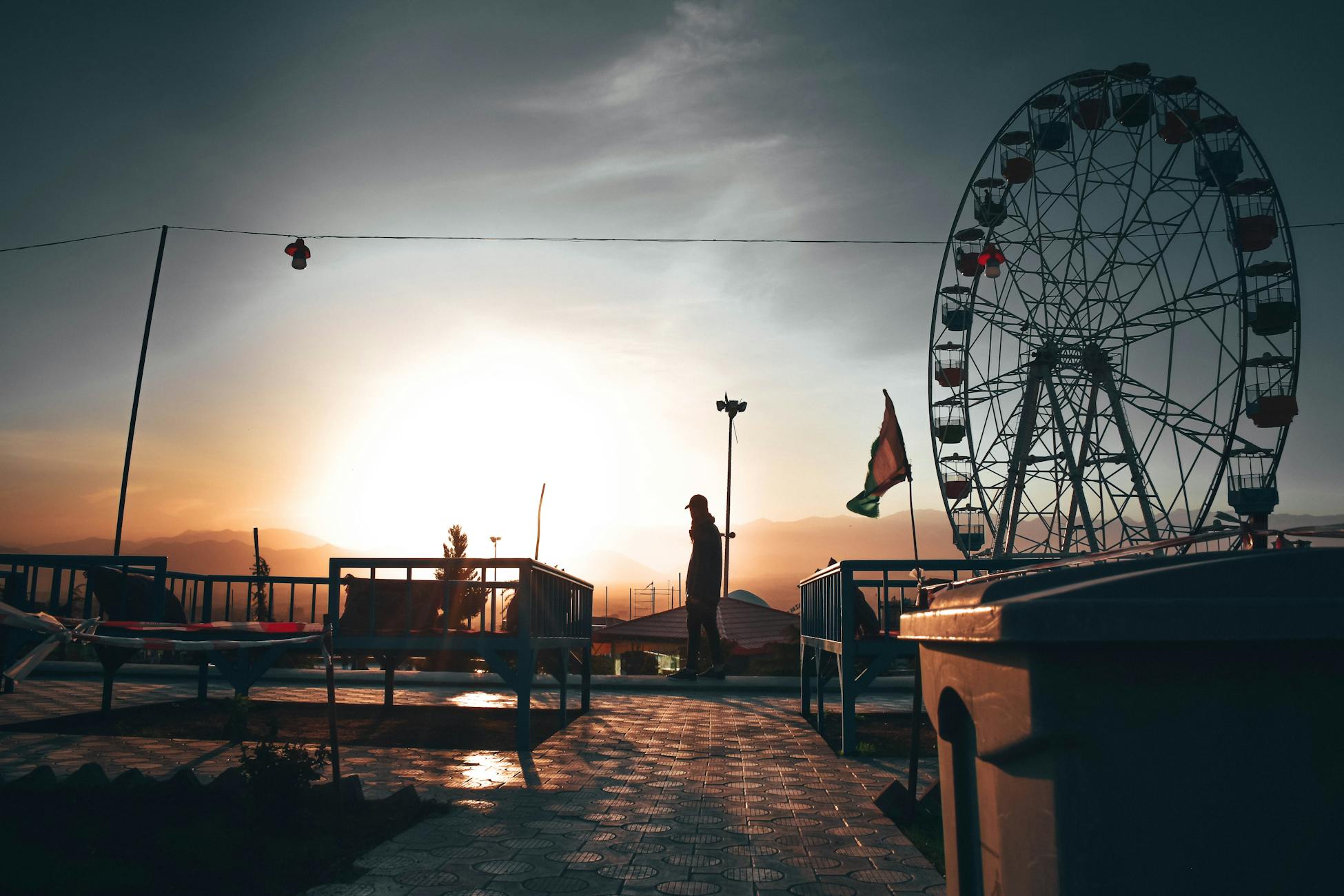 A person standing near a ferris wheel during a sunset, capturing a tranquil and scenic view.