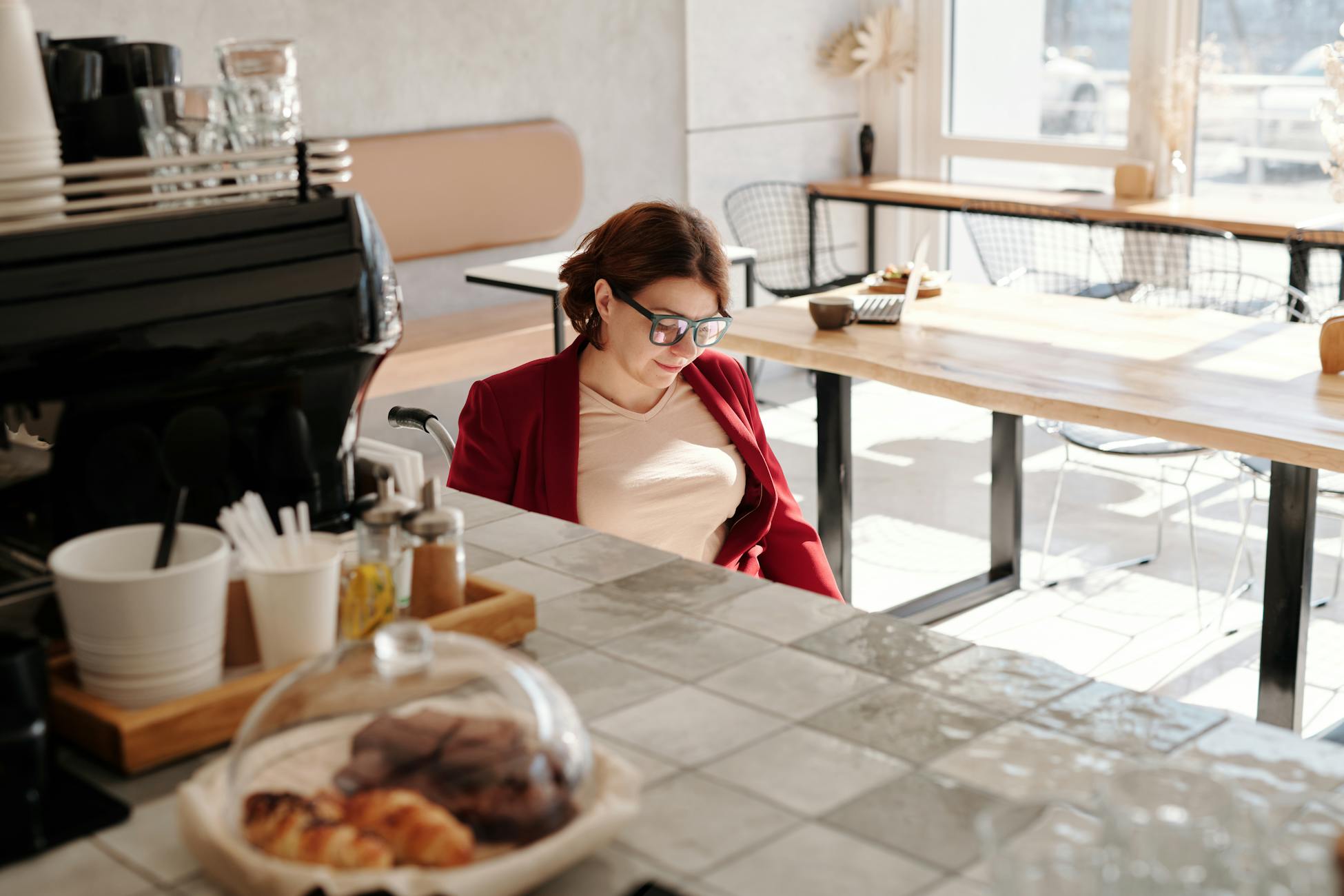 A woman in a wheelchair enjoys coffee in a sunlit café, conveying accessibility.
