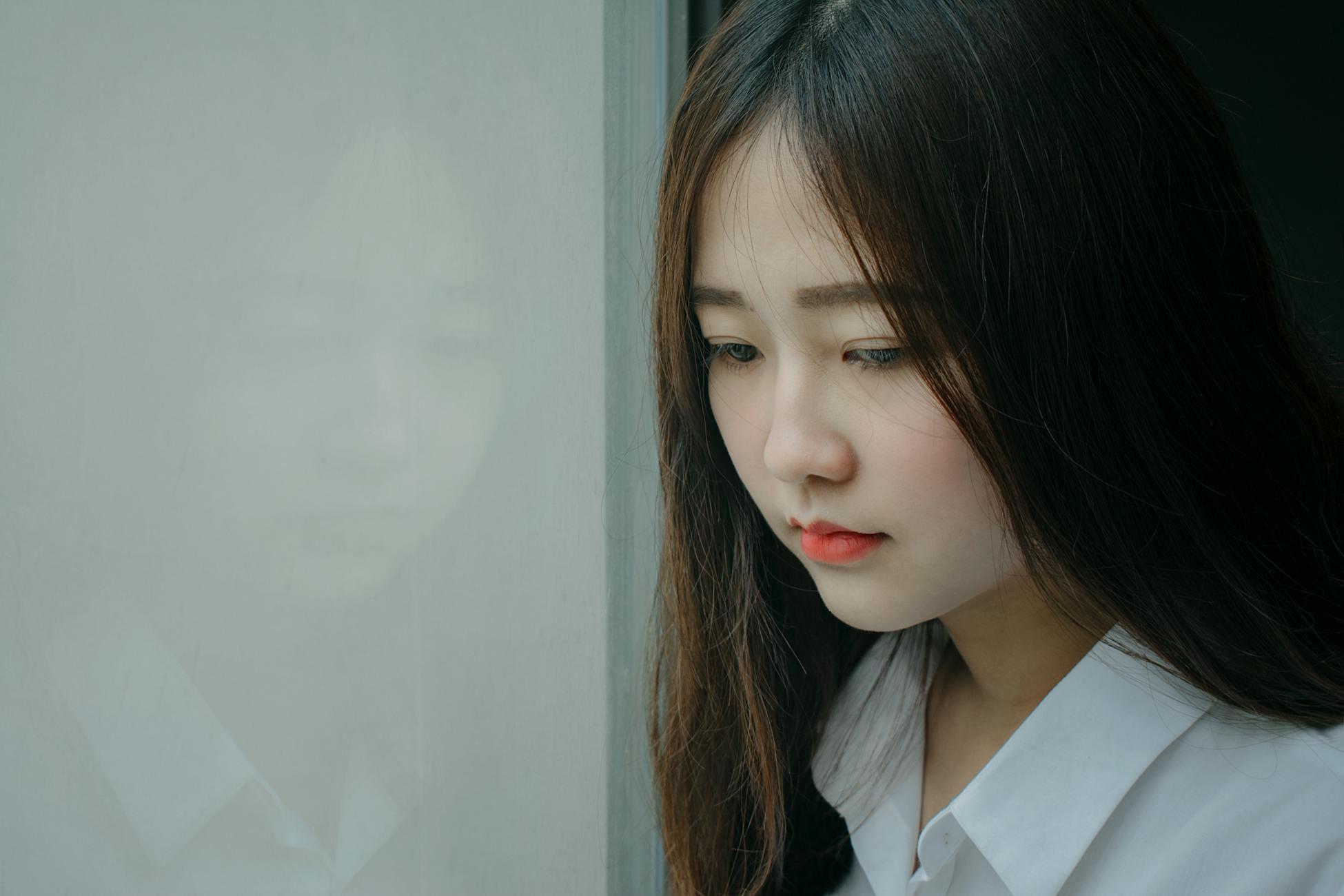 Reflective mood captured in a portrait of an Asian woman gazing outside.