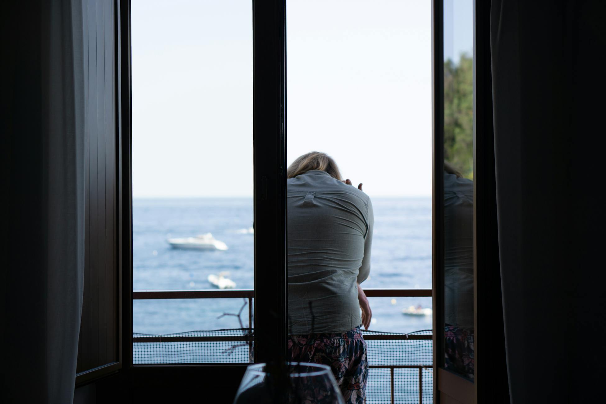A woman sits thoughtfully on a balcony overlooking the serene Campania sea, Italy.