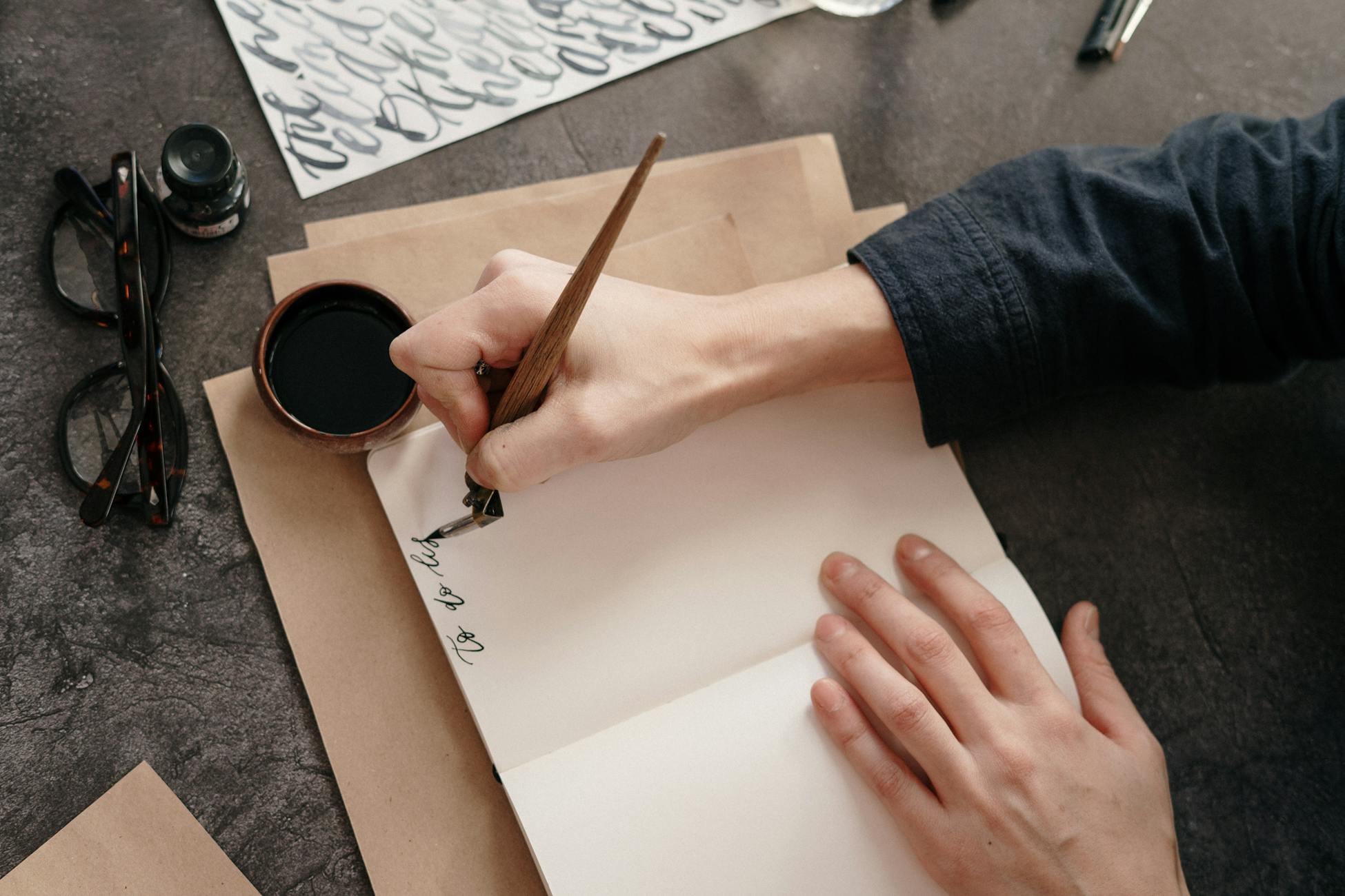 A person's hand writing calligraphy in a notebook with ink and pen, showcasing artistic skill.