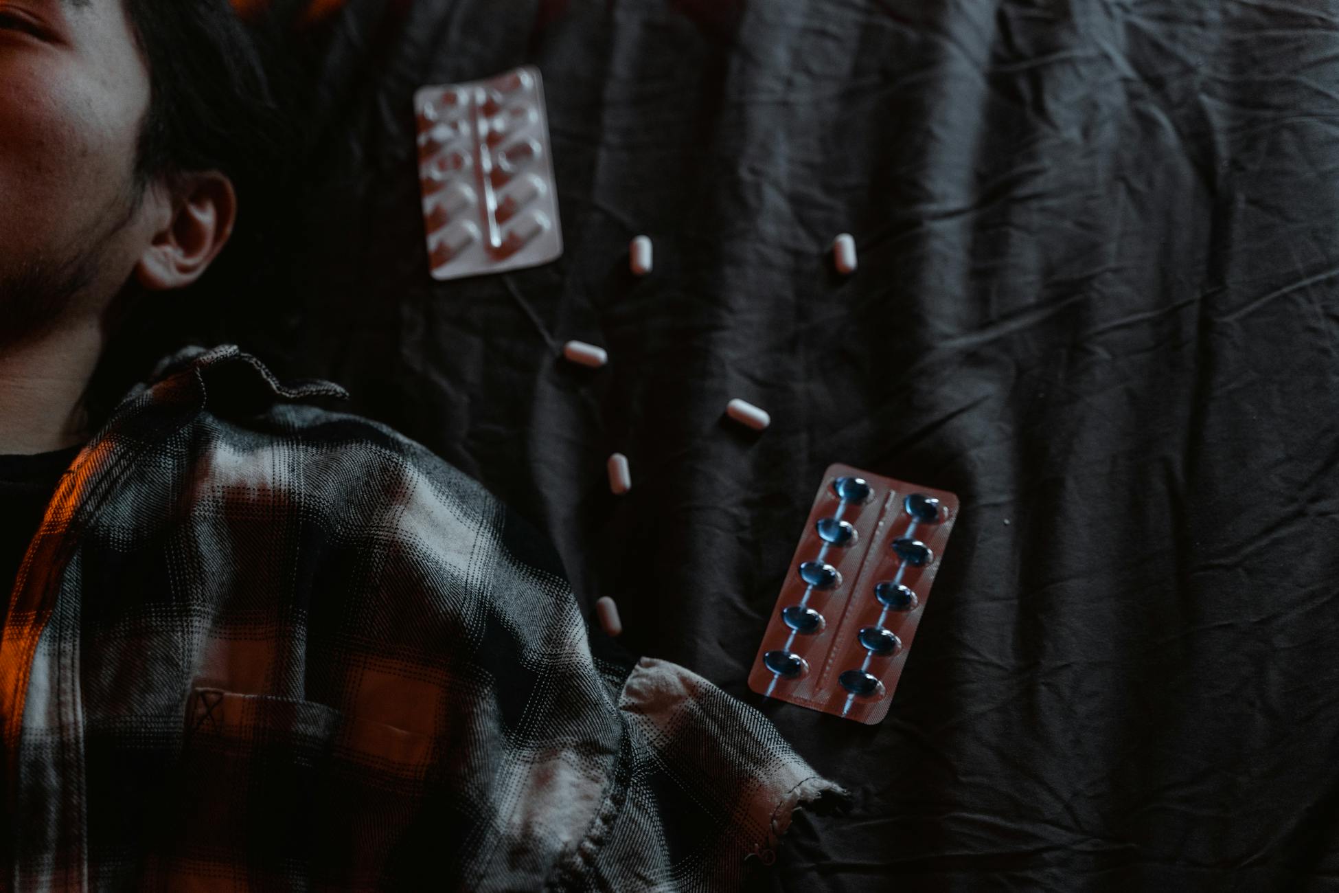 Moody portrait of a man lying next to scattered tablets, expressing distress.