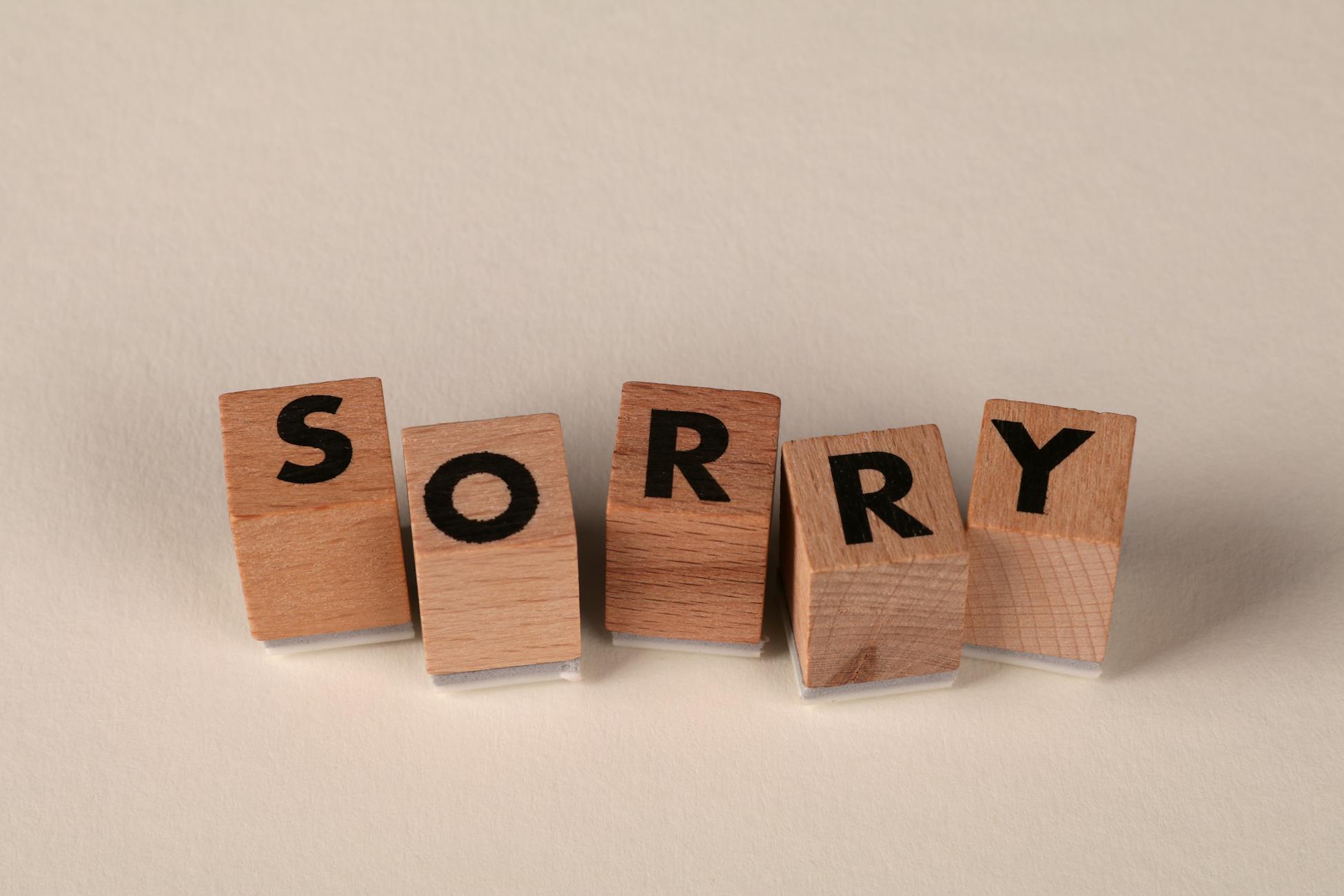 Wooden blocks arranged to spell 'Sorry' on a light, neutral background.