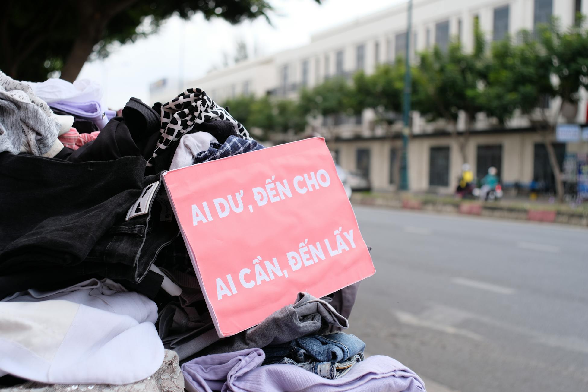 Clothes donation on city street with sign offering free items to those in need.