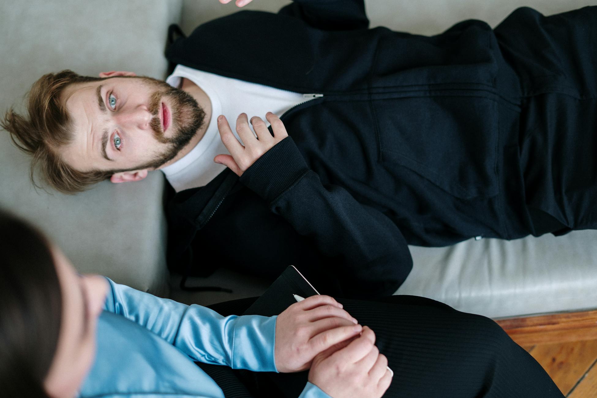 A man lying on a couch during a therapy session with a counselor in a modern office setting.