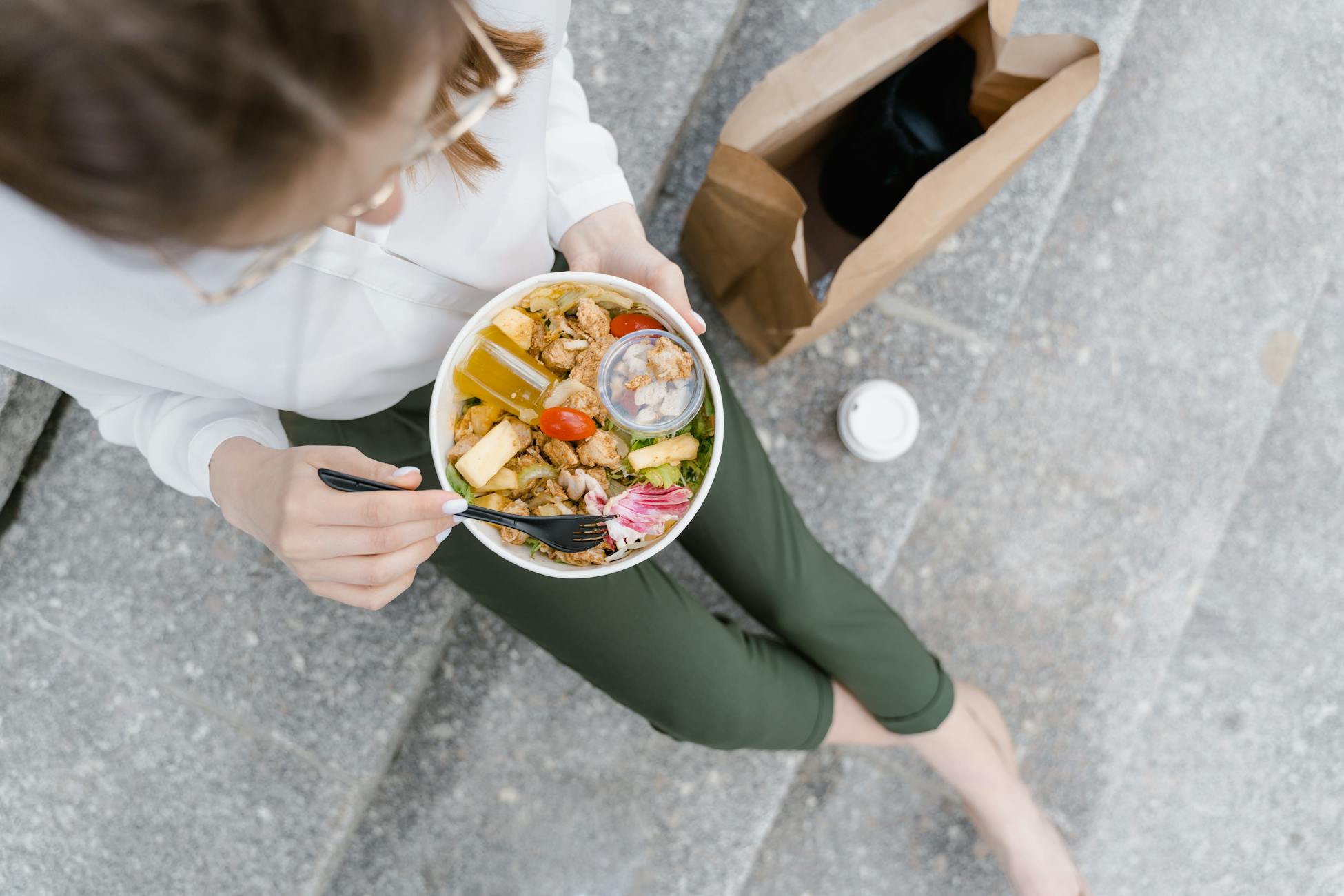 Top-down view of a woman enjoying a healthy salad outdoors during a casual lunch break.