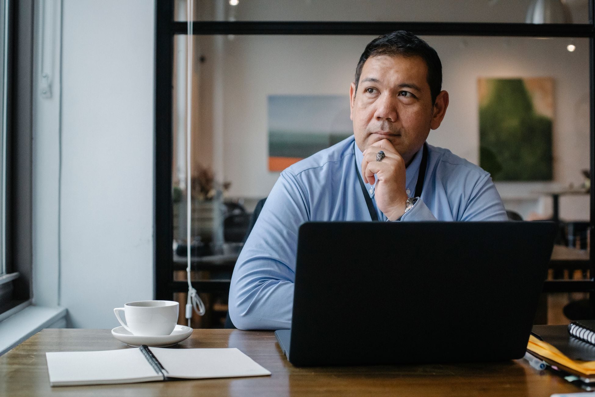 Concentrated ethnic adult male entrepreneur thinking on project while working at table with netbook and cup of drink